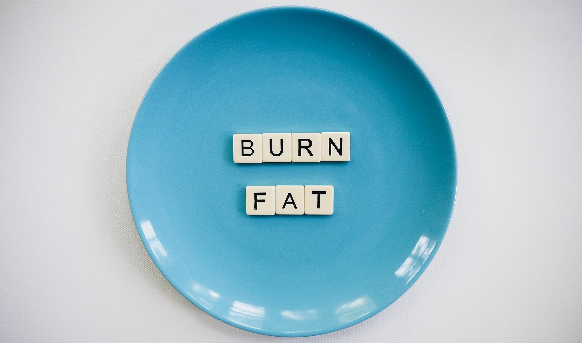 Scrabble tiles spelling Burn Fat on a blue plate, representing the fat-burning benefits of rucking